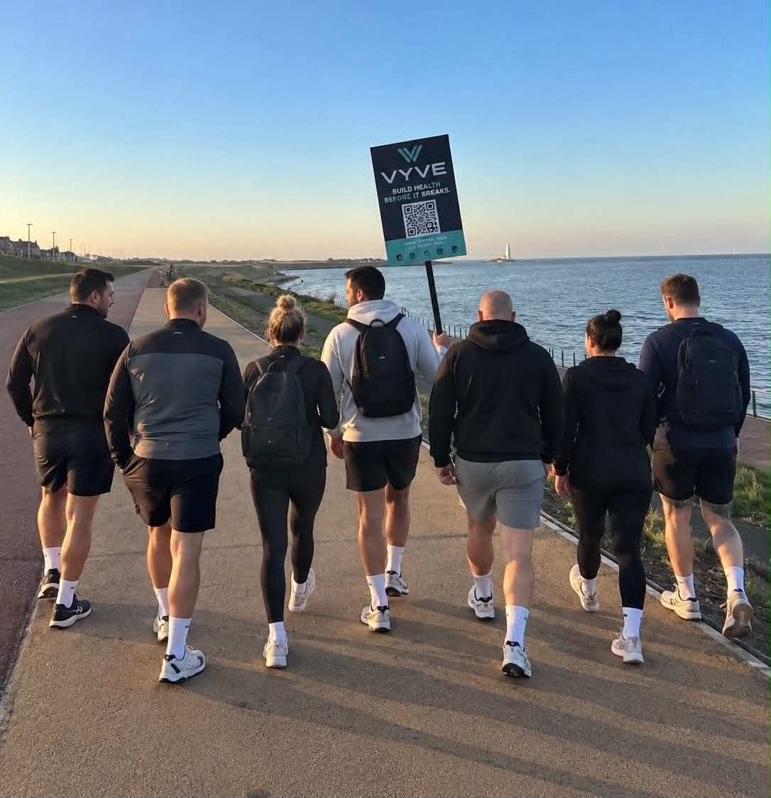The VYVE community on a coastal walk, carrying a Build health before it breaks sign